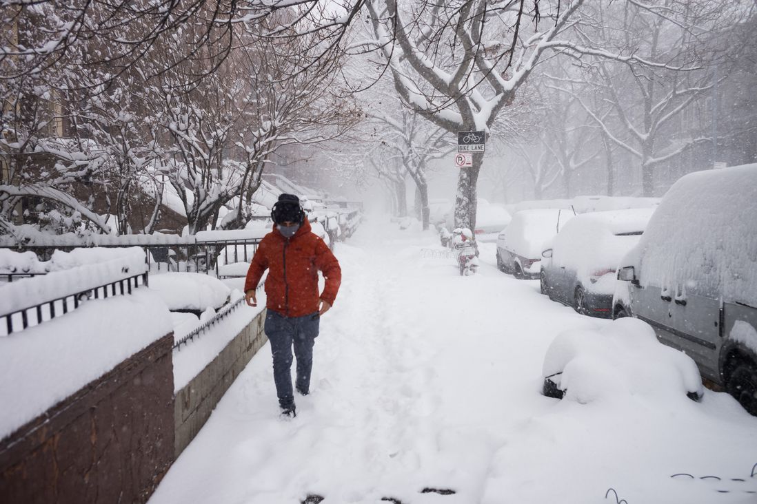A man in a red jacket and black leggings jobs on a snowy brownstone Brooklyn Street
